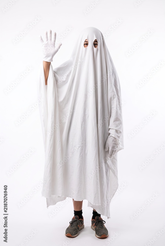 Obraz premium A person dressed as a ghost is waving their hand. The setting has an autumn theme, with a simple white background. The ghost costume is made of a white sheet with a friendly gesture