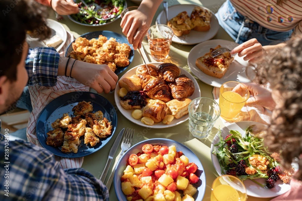 Fototapeta premium Teen friends sharing food and drinks together at sunny brunch table