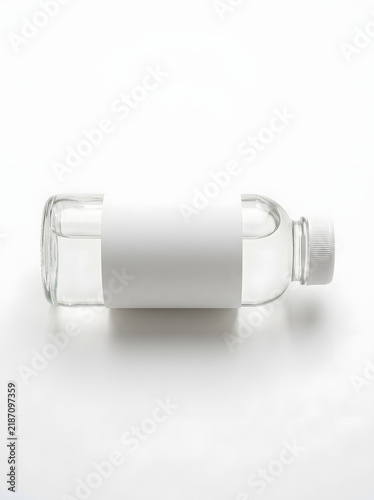 Clear glass cylindrical bottle lying on white surface with cap