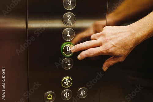 Obraz na płótnie Man hand pressing a glowing ground floor zero button on a modern metal elevator control panel inside an office building or hotel close up view