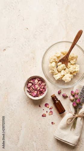 Overhead view of natural ingredients for homemade skincare products, including shea butter, dried rose petals, essential oil, and lavender.