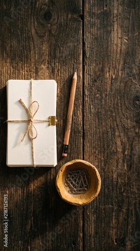 A stack of white paper tied with twine, a pencil, and paper clips on a rustic wooden table.