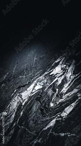Close-up of a dark, rugged rock formation with sharp, angular facets and metallic-like streaks, showcasing a complex geological texture.