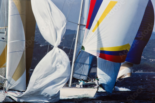 Foto High energy action of competitive sailing regatta with yachts racing under spinnaker sails, coastal landscape in background