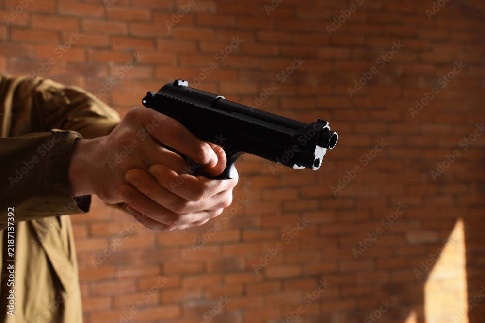 Obraz premium Gun violence and crime prevention, person holding a handgun in a tactical stance for self defense or law enforcement training against a brick wall