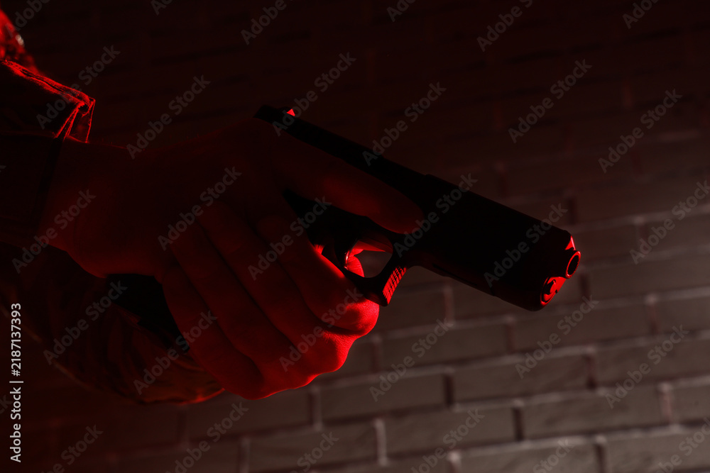 Obraz premium Gun violence and crime prevention, person holding a handgun in a dark room with red emergency lighting for security and law enforcement investigation