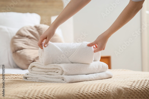 Hospitality and hotel service  housekeeper folding fresh white towels on a bed for guest comfort and room preparation in a modern bedroom interior