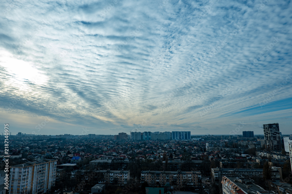 Fototapeta premium textured altocumulus clouds over city skyline, wave cloud formation above residential urban landscape, scenic sky with ripple clouds over city buildings