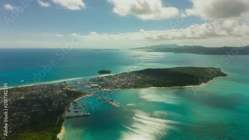 Aerial view of a bustling coastal town with a marina and tropical islands.
