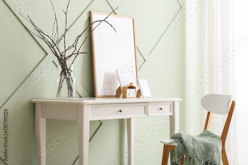 Vase with tree branches and frames on table near green wall in room