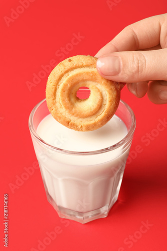 Фотография Hand dipping tasty spritz biscuit in glass of milk on red background