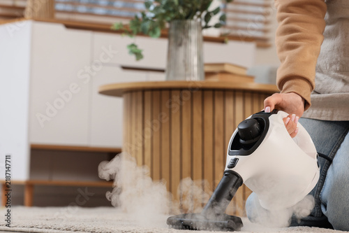 Woman steam cleaning carpet in room