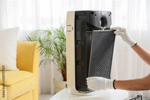 Young female worker changing filter in modern air purifier at home, closeup