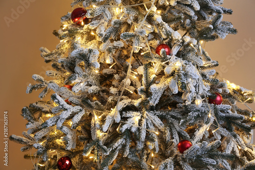 Фотография Decorated Christmas tree with glowing lights near beige wall, closeup
