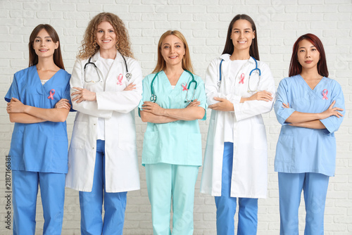Female doctors with pink ribbons on white brick background. Breast cancer awa...