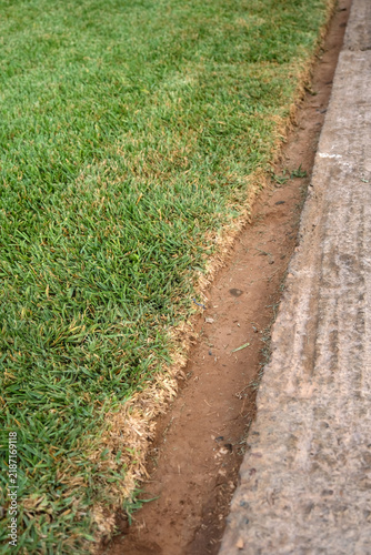 Canvastavla Well maintained green lawn with a neatly trimmed edge bordering an earthen strip and stone walkway, illustrating professional landscape care