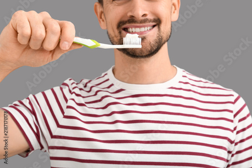 Handsome man brushing teeth on grey background, closeup