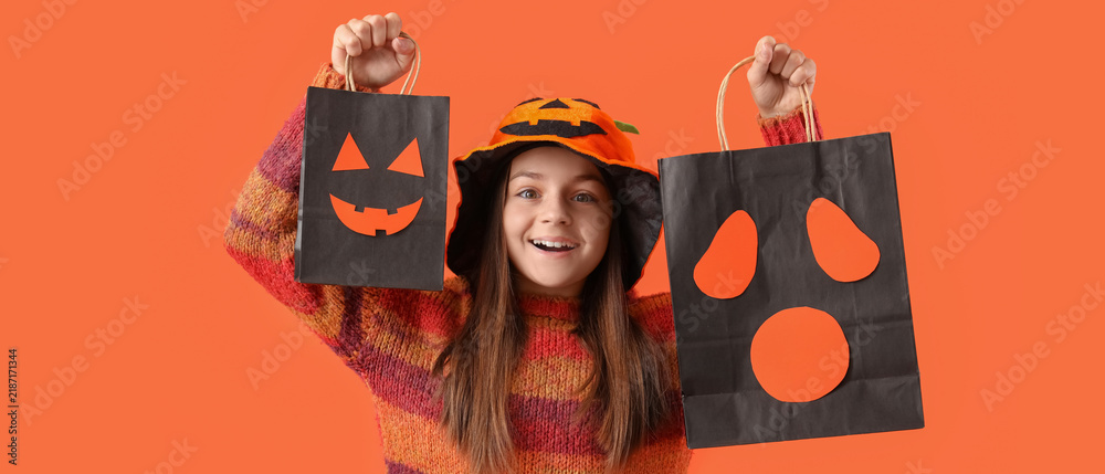 Obraz premium Halloween celebration and trick or treat, happy girl holding paper bags with spooky faces and wearing pumpkin hat on a bright orange background