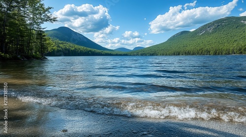 Tranquil lake reflects majestic mountains, clear blue sky, and fluffy clouds, showcasing natural beauty and outdoor serenity