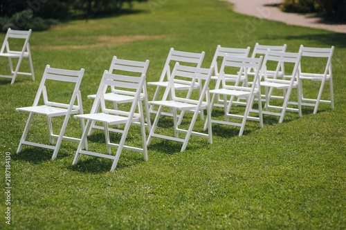 Foto Photo of white wooden folding chairs on green grass in outdoor park at wedding ceremony