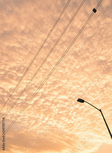 Orange sunset sky with clouds, power lines and street lamp, warm evening atmosphere, urban infrastructure silhouette against bright sky, peaceful and scenic outdoor view