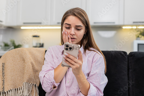 Bild auf Leinwand Young woman at home holds smartphone reads result and sighs after game loss and work rejection