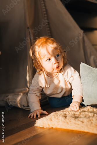 Curious toddler crawling on the floor and exploring a cozy home interior illuminated by warm natural sunlight. Candid childhood lifestyle moment at home.