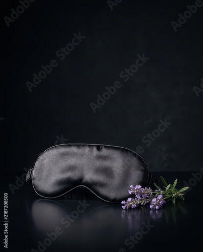 Luxury black silk sleep mask with fresh lavender on dark reflective surface for wellness advertising