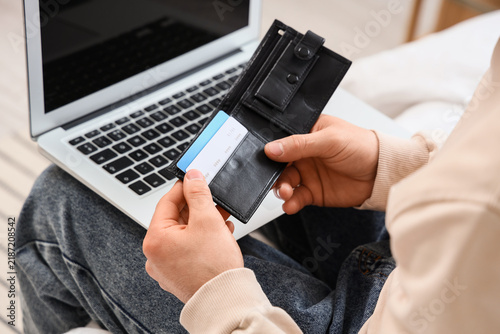 Man with wallet and credit cards using laptop in bedroom, closeup