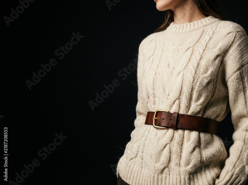 Elegant fall fashion advertising with leather belt on textured knit sweater and copy space on black.