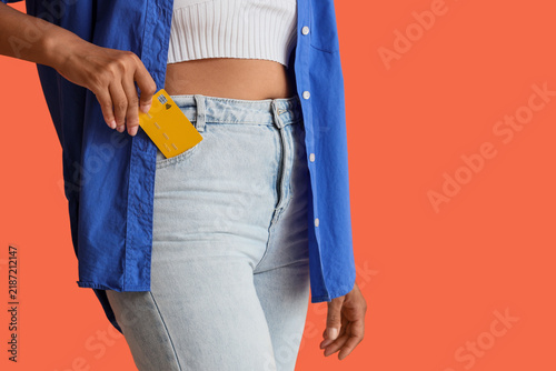 Young woman with credit card in her pocket on orange background, closeup