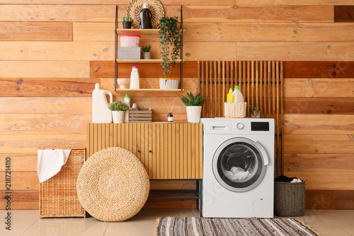 Modern washing machine, chest of drawers and shelving unit near wooden wall i...