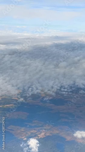 View from an airplane window showing clouds and land below. 