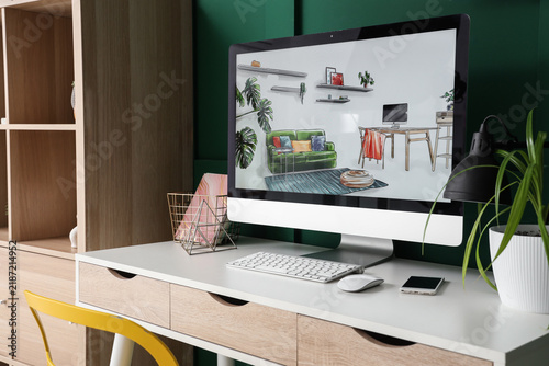 Interior designers workplace with computer and plant near green wall in office