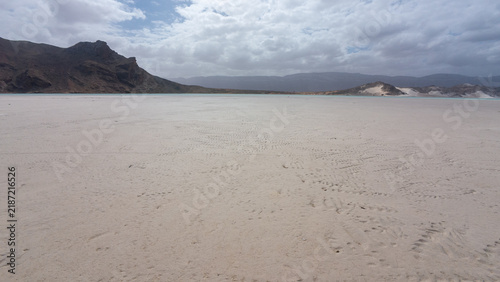 Canvastavla Empty white sand beach beneath rocky mountains