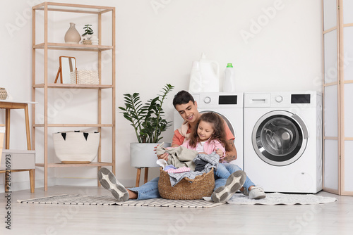 Young father and his daughter with laundry basket sitting near washing machin...