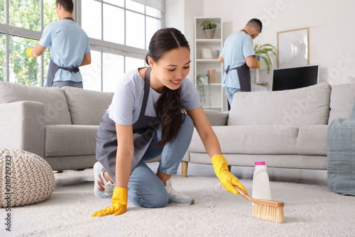 Female Asian janitor cleaning carpet with brush in room