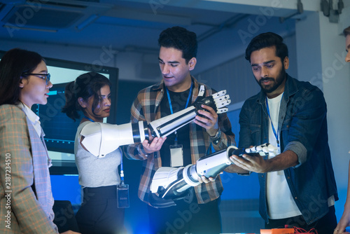 A diverse team gathers in a modern tech workshop to test and assemble advanced robotic prosthetic limbs, collaborating on engineering projects together under cool indoor lighting.