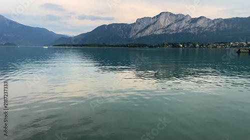 Peaceful panoramic view of Lake Mondsee in Austria at sunset, with calm water reflecting the evening sky and majestic Alpine mountains. Serene summer scenery in the Salzkammergut region