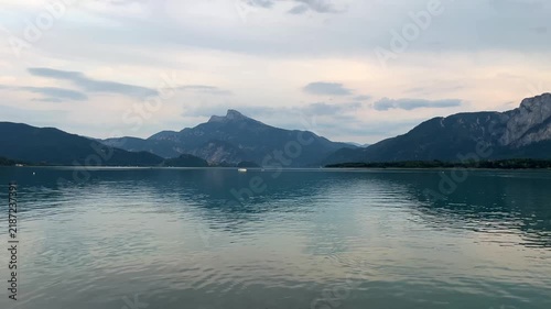 Peaceful panoramic view of Lake Mondsee in Austria at sunset, with calm water reflecting the evening sky and majestic Alpine mountains. Serene summer scenery in the Salzkammergut region