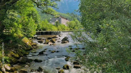 Mountain river with rushing rapids and small cascades in Lofer, Austria, surrounded by lush green forest and Alpine mountains. Peaceful summer nature landscape with flowing water.