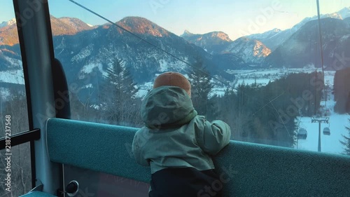 Young child riding a cable car at Almenwelt Lofer in Austria, looking at snowy Alpine mountains through the window during sunset. Cozy winter family travel scene in the Austrian Alps