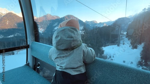 Young child riding a cable car at Almenwelt Lofer in Austria, looking at snowy Alpine mountains through the window during sunset. Cozy winter family travel scene in the Austrian Alps