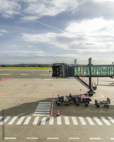 Gdansk, Wojewodztwo pomorskie, Poland - 07 September 2026: View of Gdansk Lech Walesa Airport with a jet bridge over the tarmac and luggage carts parked nearby under a cloudy sky.