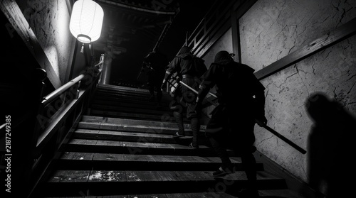 Ninjas in black stealth gear climb stairs at night holding swords. Japanese shinobi warriors infiltrate an ancient wooden fortress. Feudal warrior concept ideal for historical and cinematic projects.