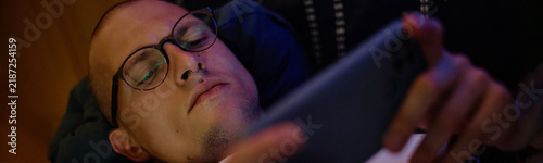 Obraz na plátně Young adult Caucasian man wearing glasses lying down and playing video games on smartphone