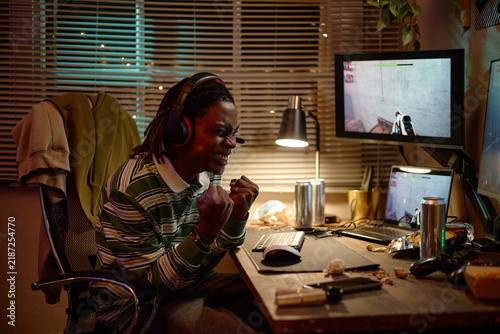 Fotografía Young adult African American man wearing headset playing video games on computer and celebrating victory