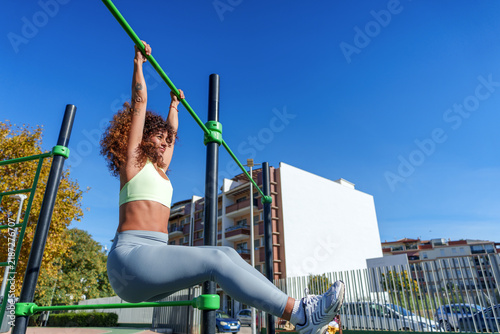 Obraz na płótnie Young woman performing hanging leg raises in outdoor calisthenics park, building