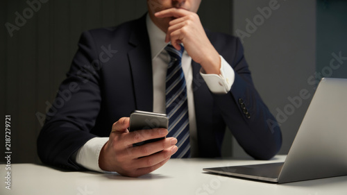 Businessman in a suit holding a smartphone at a desk with a laptop with smartphone while looking professional man formal suit tie sits communication work