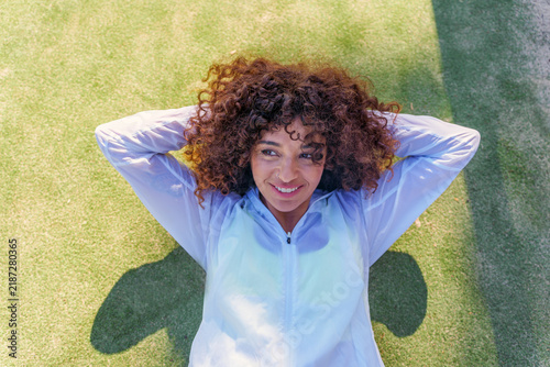 Фотография Woman with curly hair resting on artificial grass after exercise, feeling relaxe